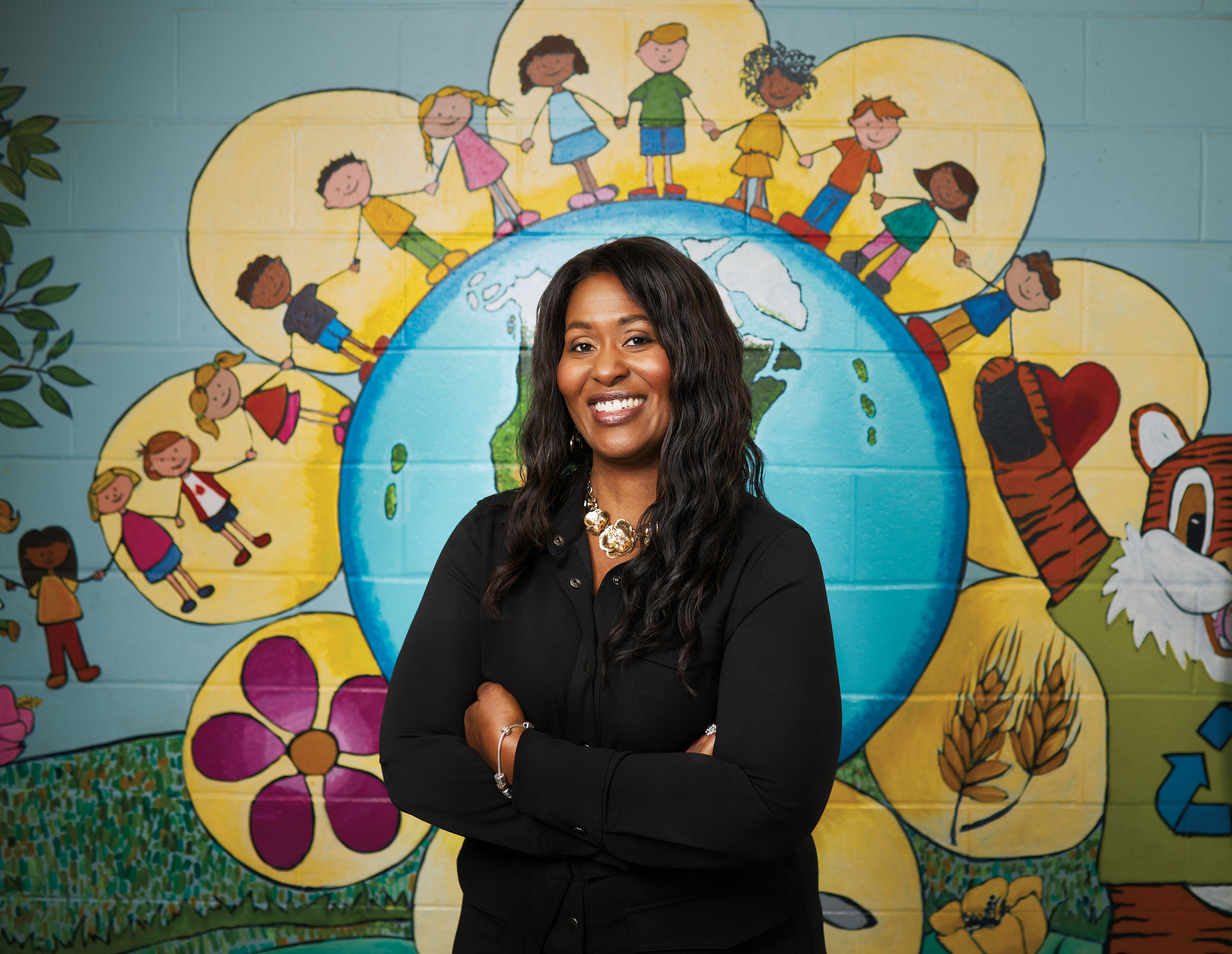 Judette Dumel, enseignante agréée de l’Ontario, debout devant une murale peinte représentant des enfants autour de la Terre se tenant la main.