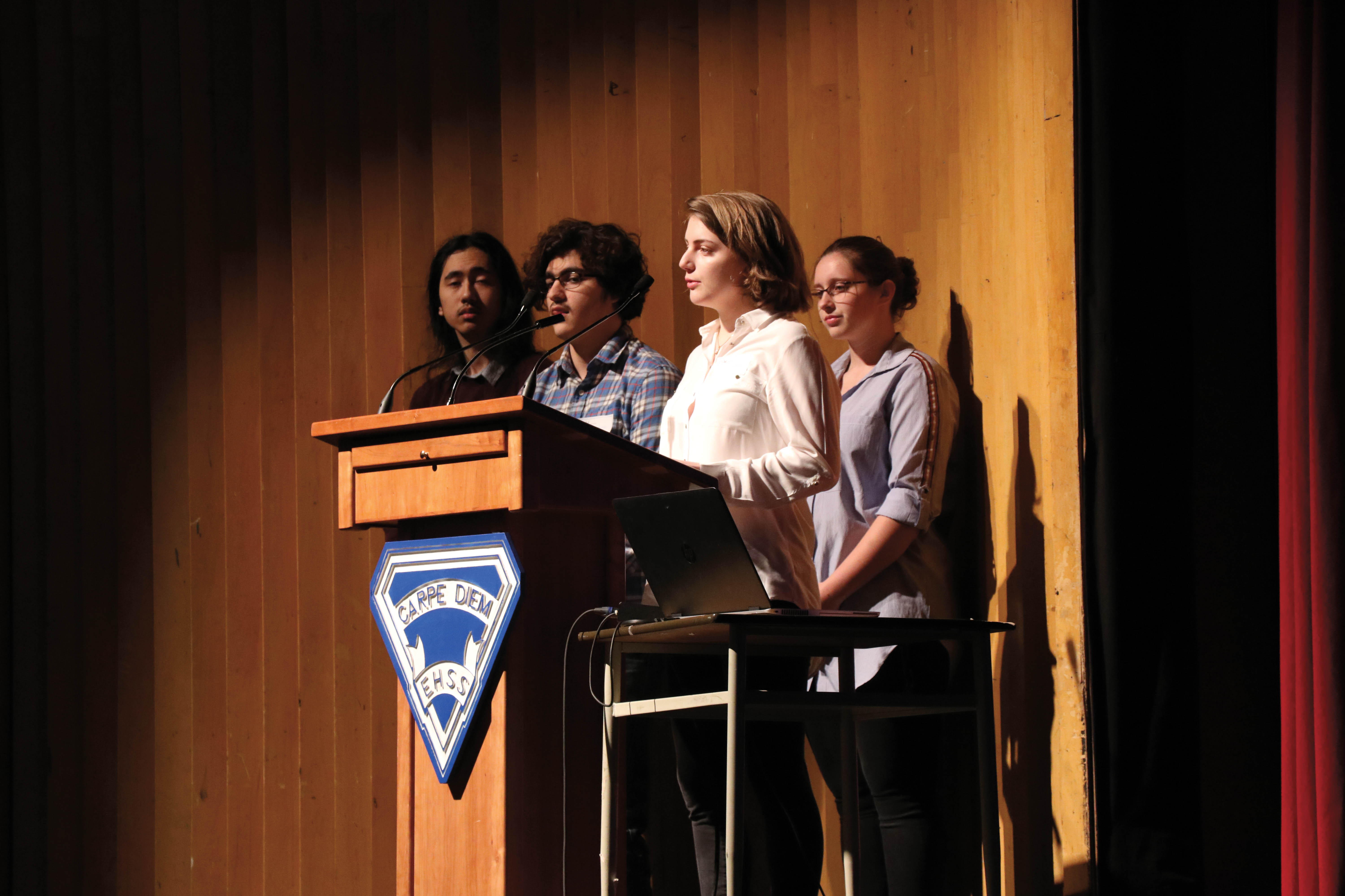 A photo of four students at a podium in an auditorium